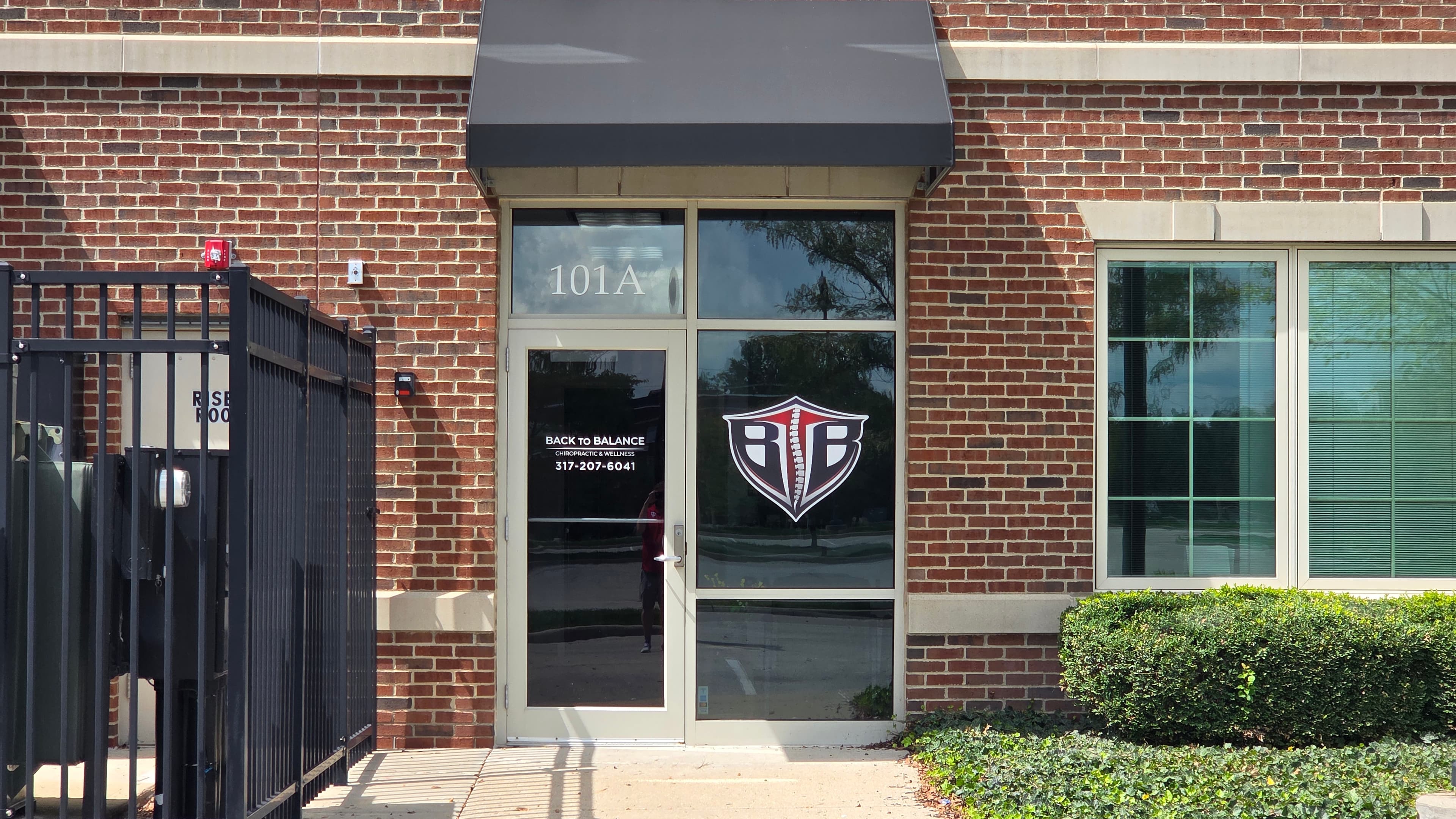 Close-up of Suite 101A entrance door with black awning, 101A transom, phone number, and shield logo